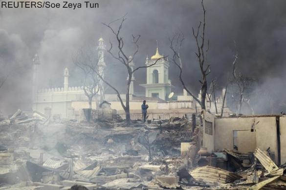 A man stands in front of a mosque as it burns in Meikhtila, March 21, 2013