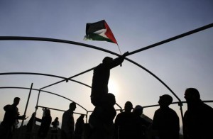 A man hangs a Palestinian flag as others erect a tent at a land that they said was confiscated by Israel, during a protest against land confiscations near the West Bank town of Abu Dis