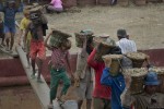 In this June 10, 2014 photo, Chit Toke, wearing an oversized green trouser walks in a narrow timber beam hauling a basket of gravel, weighing about 19 kilograms (42 pounds) in Yangon, Myanmar. He receives 35 kyats ($0.037) for hauling a basket full of gravel from a boat to shore, walking a distance of about 30 meters (100 feet). Early every morning, 11-year-old Chit Toke wakes up in the small bamboo shack where his family lives besides a creek. He pulls on oversized green trousers, part of a cast-off school uniform, and walks over to the riverside where boats and barges are docked to unload gravel to supply the booming construction industry in Yangon, Myanmar's biggest city and commercial capital. (AP Photo/Gemunu Amarasinghe)