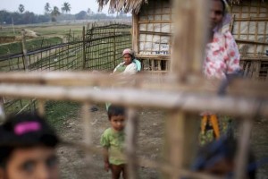 Internally displaced Rohingya women and children look from behind the fence of their temporary home at Thae Chaung IDP camp on the outskirts of Sittwe