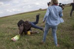 A migrant carrying a child falls after tripping on a TV camerawoman (R) while trying to escape from a collection point in Roszke village, Hungary, September 8, 2015. REUTERS/Marko Djurica